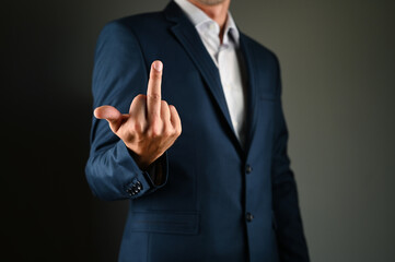 The man shows the middle finger forward. A man in a suit shows middle forward on a black background. Concept: Negative message in business.