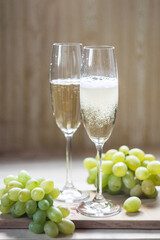 Two glasses with sparkling wine and grapes on light wooden background. Selective focus.