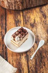 Tiramisu cake sitting on a vintage wooden table with porcelain white spoon ready for a nice brake at noon