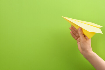 Woman holding paper plane on green background, closeup. Space for text