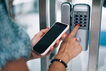 Cropped image of female holding smartphone checking code for entrance door of building, millennial woman pressing buttons entering code for security system smart home control electronic unlock