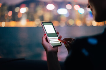 Smartphone with blank screen in hand of crop young woman on blurred night city background