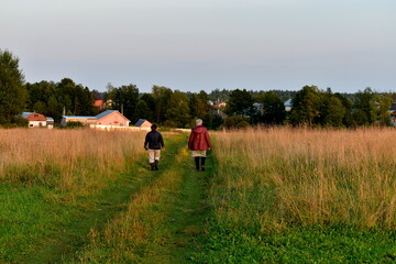 women walk to the village along a country road at sunset