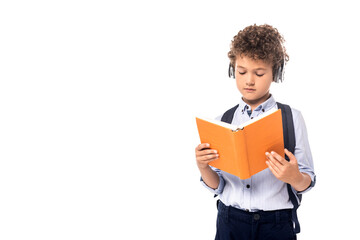curly schoolboy in wireless headphones reading book isolated on white