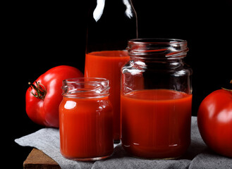 Tomato juice in glass jars on wooden table. Dark photo