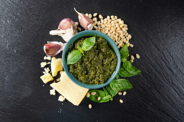 Flat lay view at green bowl with genovese pesto sauce and its ingredients in the center of slate...