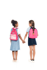 back view of multicultural schoolgirls with backpacks holding hands and standing isolated on white