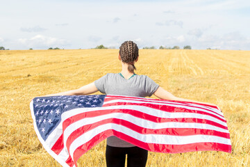 Young beautiful woman with afro-braids holding USA flag in a field.