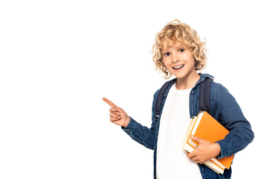 blonde schoolboy holding books and pointing with finger isolated on white
