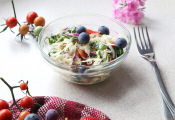 Vegetable salad with grapes in a glass dish on the kitchen table, close-up