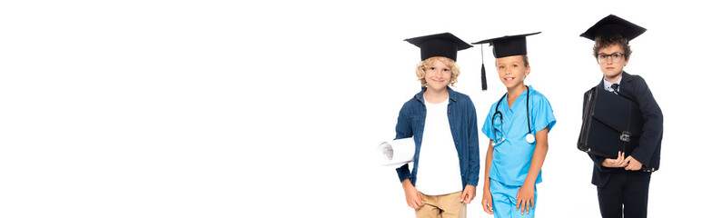 panoramic crop of children in graduation caps dressed in costumes of different professions holding blueprint and briefcase isolated on white