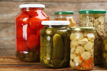 Jars of pickled vegetables on wooden table, closeup
