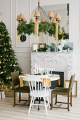 Stylish festive Christmas table with vintage chairs near the marble fireplace and Christmas tree in the living room or dining room in the house