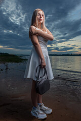 A girl in a white dress stands on the beach in the evening