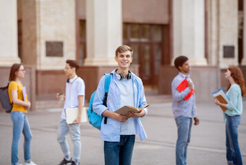 Student Standing With Book And Backpack Posing Near College Building