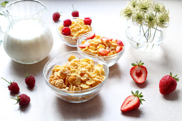 Delicious quick Breakfast of raspberries and strawberries and cornflakes, milk in a decanter, a bouquet of flowers on the kitchen table, close-up