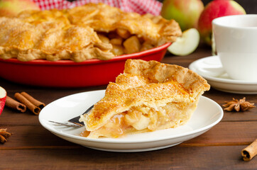Slice of classic American apple pie with cinnamon on a white plate on a dark wooden background. Rustic style. Copy space.