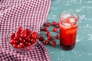 Cornel berries in a bowl with drink high angle view on plaster and picnic cloth background