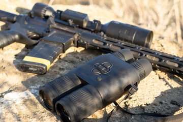 A rifle with a telescopic sight and binoculars on a stone background. Hunting and observation technologies