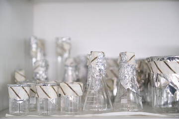 Sterile laboratory glassware with aluminum foil and autoclave tape. Real laboratory material.