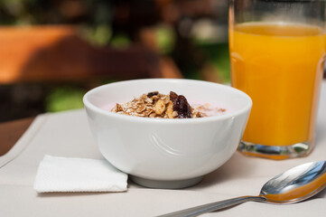 Yogurt and granola for a breakfast meal in a white bowl and a glass of orange juice 