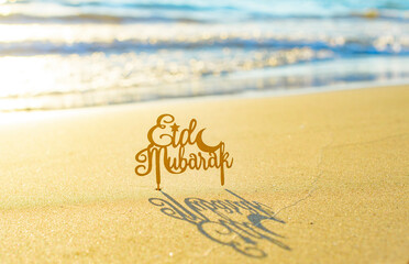 text Eid Mubarak (in English Happy Holidays) on the sand by the sea