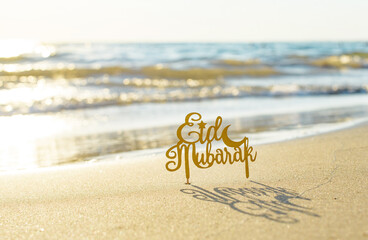 text Eid Mubarak (in English Happy Holidays) on the sand by the sea