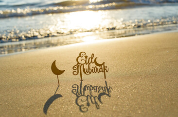 text Eid Mubarak (in English Happy Holidays) on the sand by the sea