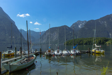 Fototapeta na wymiar Yachts and boats in a small port on an Alpine lake, cliffs and mountains in background. Travel picturesque landscape. Yachting on sunny day.Summer vacation travel holiday design.Adventure outdoors