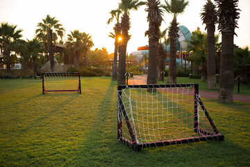 Empty small kids soccer field on vacation at sunset with beautiful green grass. Palm trees in the background. Football. Leisure. Active games. sport. Relax. Weekend. Bright setting sun. Resort © Катерина Бухвалова