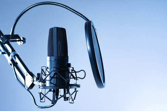 Close-up Studio condenser microphone with pop filter and anti-vibration mount for live recording. Microphone with a pop filter on a gray background. Studio microphone and text space. - Powered by Adobe