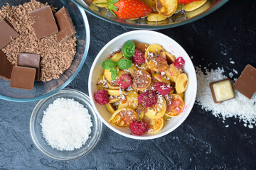 mini pancake cereal bowl with fresh strawberries banana chocolate, coconut shavings and honey in small plates. the view from the top . the trend of self-isolation