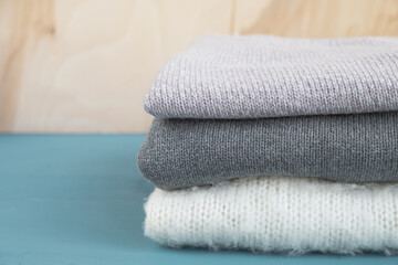 Knitted sweaters on blue wooden table. Warm autumn or winter clothes. Close up, copy space