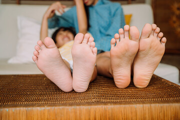 little child and mother barefooted feet on a bed.