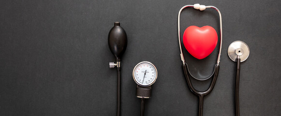 Medical stethoscope and sphygmomanometer on black background, top view.