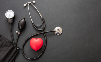 Medical stethoscope and sphygmomanometer on black background, top view.