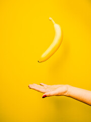 Female hand with fresh ripe banana on yellow background.