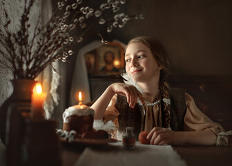 A girl with a pen in her hand looks towards the window. Portrait of a girl painting eggs on the background of icons. Preparing for Easter in Russia.