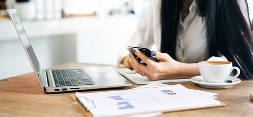 Close up young businesswoman using mobile phone and laptop working with paperwork of investment on desk