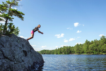 Girl leans, just about to jump off a rock into a lake