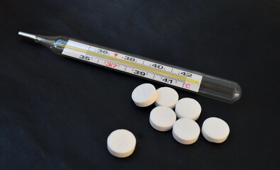 Thermometer and a handful of white pills. Disease prevention.