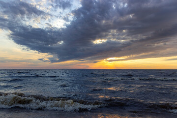 Obraz premium Stormy sea with sunset sky and orange-yellow sun through the clouds over. Meditation at the ocean and sky background. Tranquil seascape. Horizon over the water. Useful for design and place for text.
