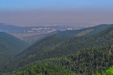 Landscape with green trees mountains and a view of a polluted gray city in smoke, dirty air