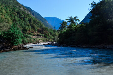 A mountainous blue river flows between hills and mountains covered with green trees and bushes