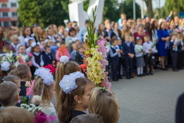 A solemn line of first-graders dedicated to entering the primary school of Minsk, Belarus in the background. Flowers are in the foreground.