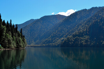 Fototapeta na wymiar Beautiful blue clear emerald Lake Ritsa in Abkhazia glowing in the sun near the middle of high green trees mountains