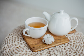 Fototapeta na wymiar A mug of hot tea, a teapot, a wooden stand on an ottoman. Cozy autumn. Winter breakfast. Cotton.