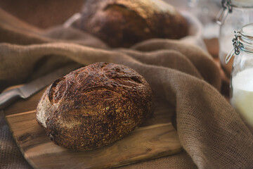 Freshly baked sourdough wheat bread laying on wooden board covered with jute.