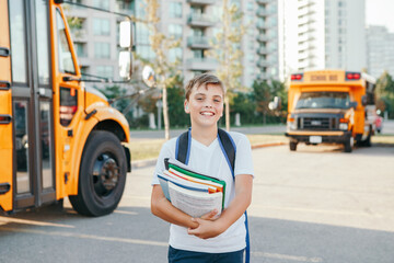 Happy Caucasian boy student with backpack and exrecise books near yellow bus on first September...