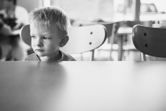 a little boy sitting at an empty table looking grumpy